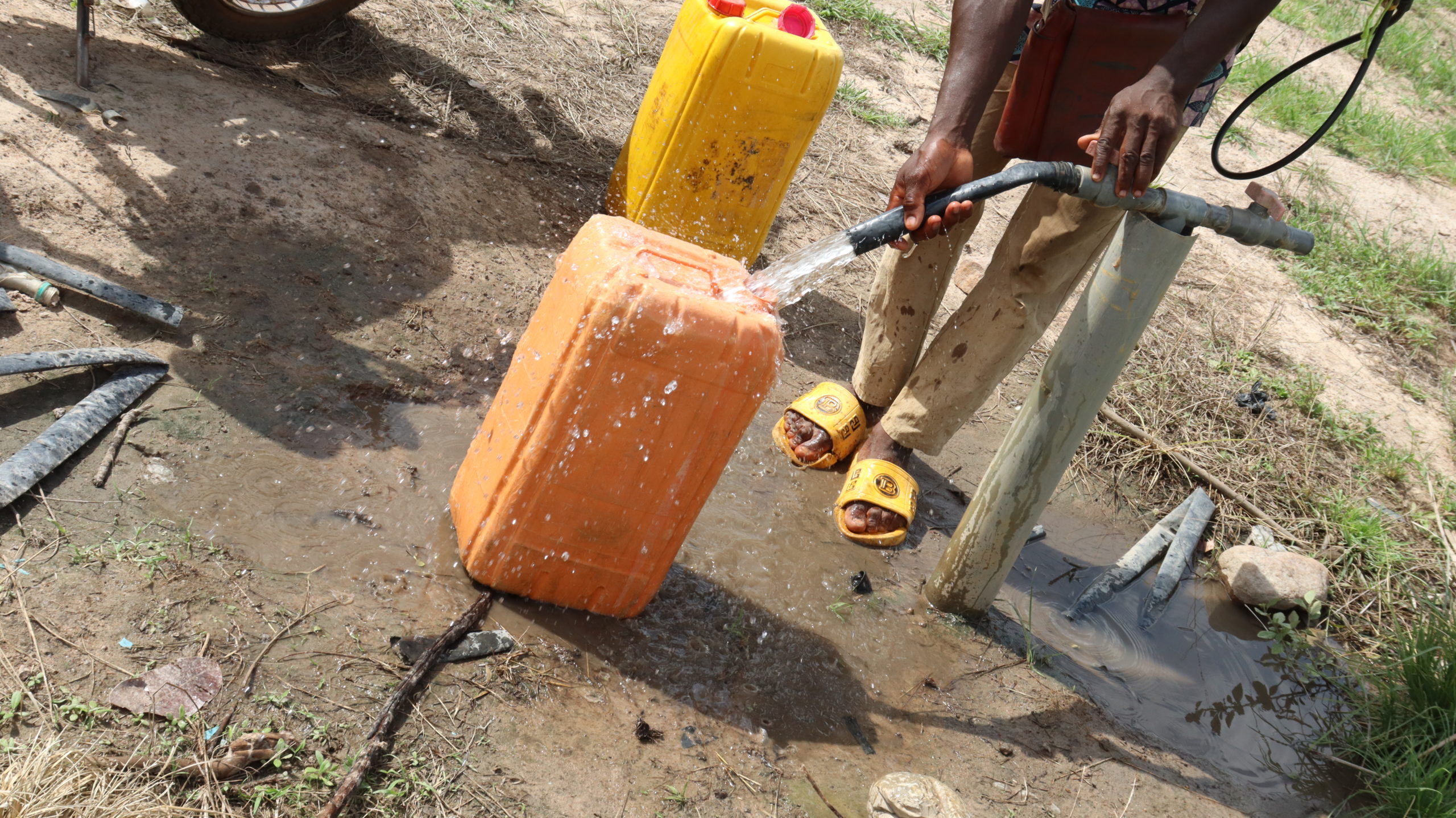 Deux bidons remplis à la main à un point d'eau, sur un site maraîcher du nord du Bénin.